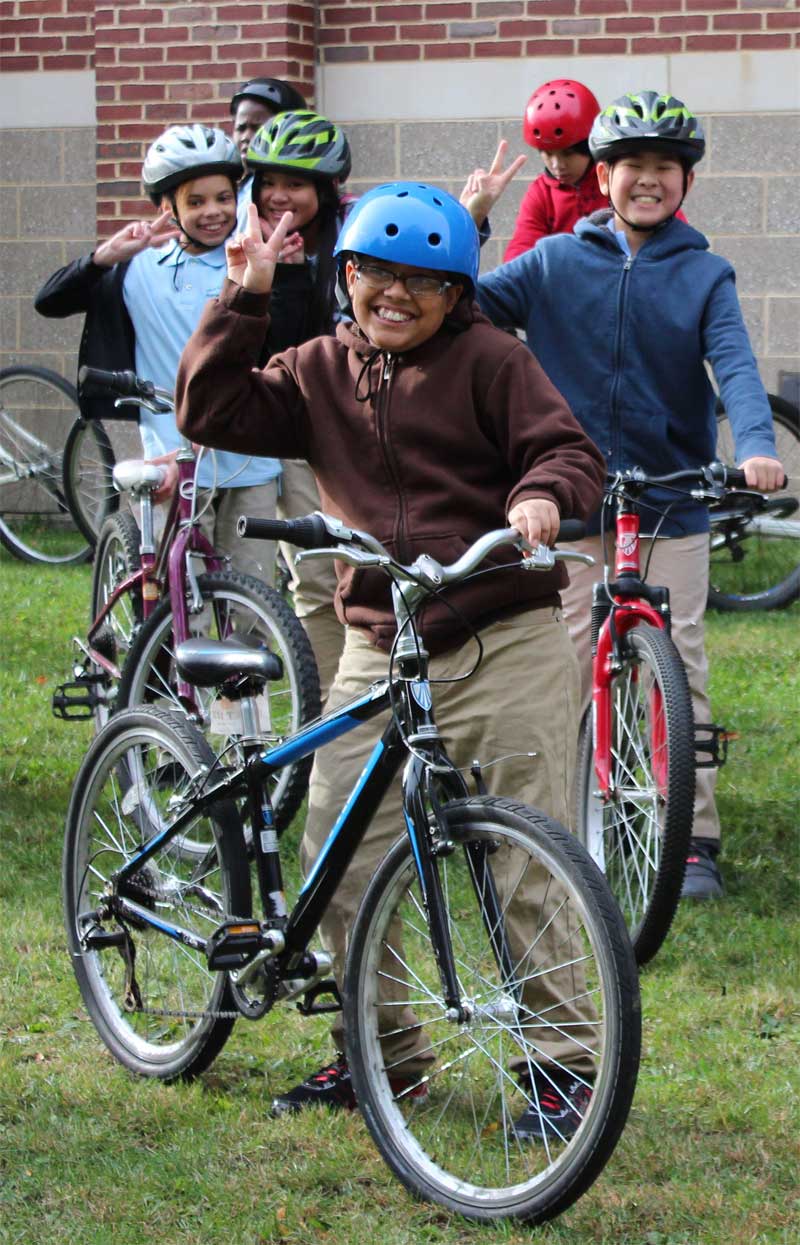 Image for a group of youth with bicycles and wearing helmets smile at the camera 