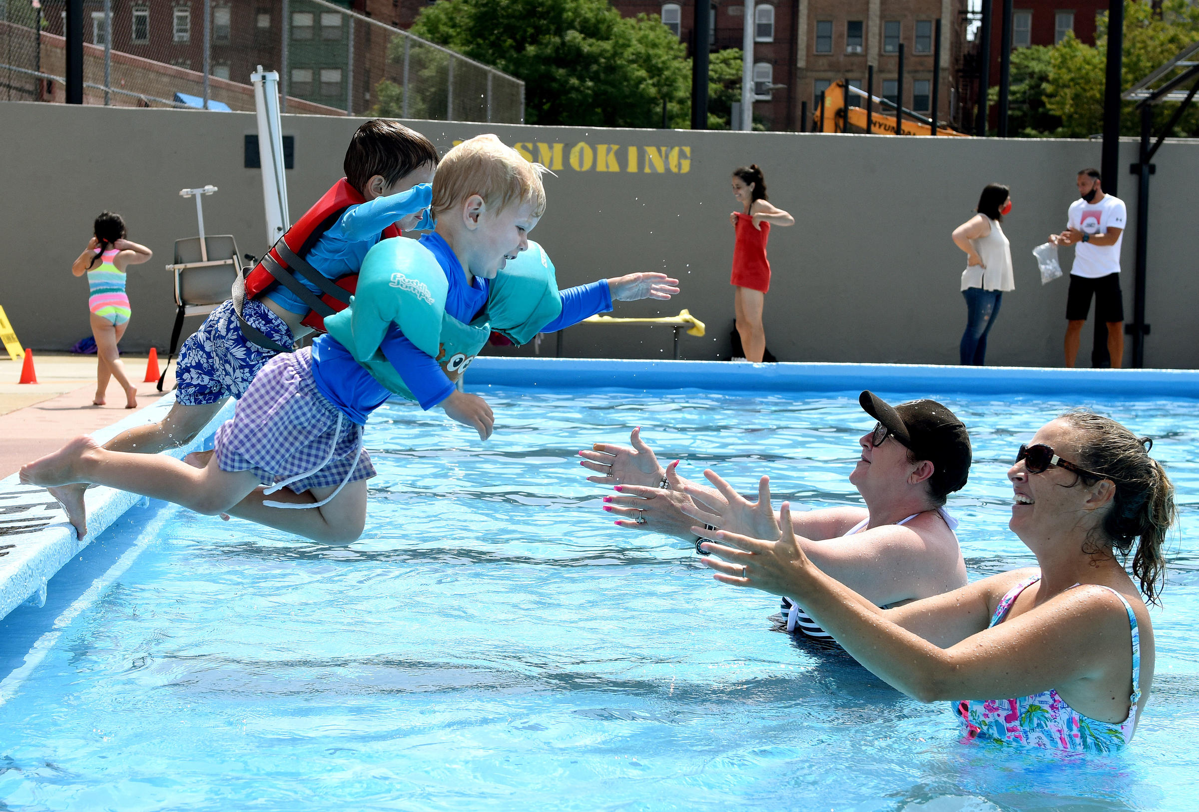 Two kids jump into the pool, into the arms of two adults.