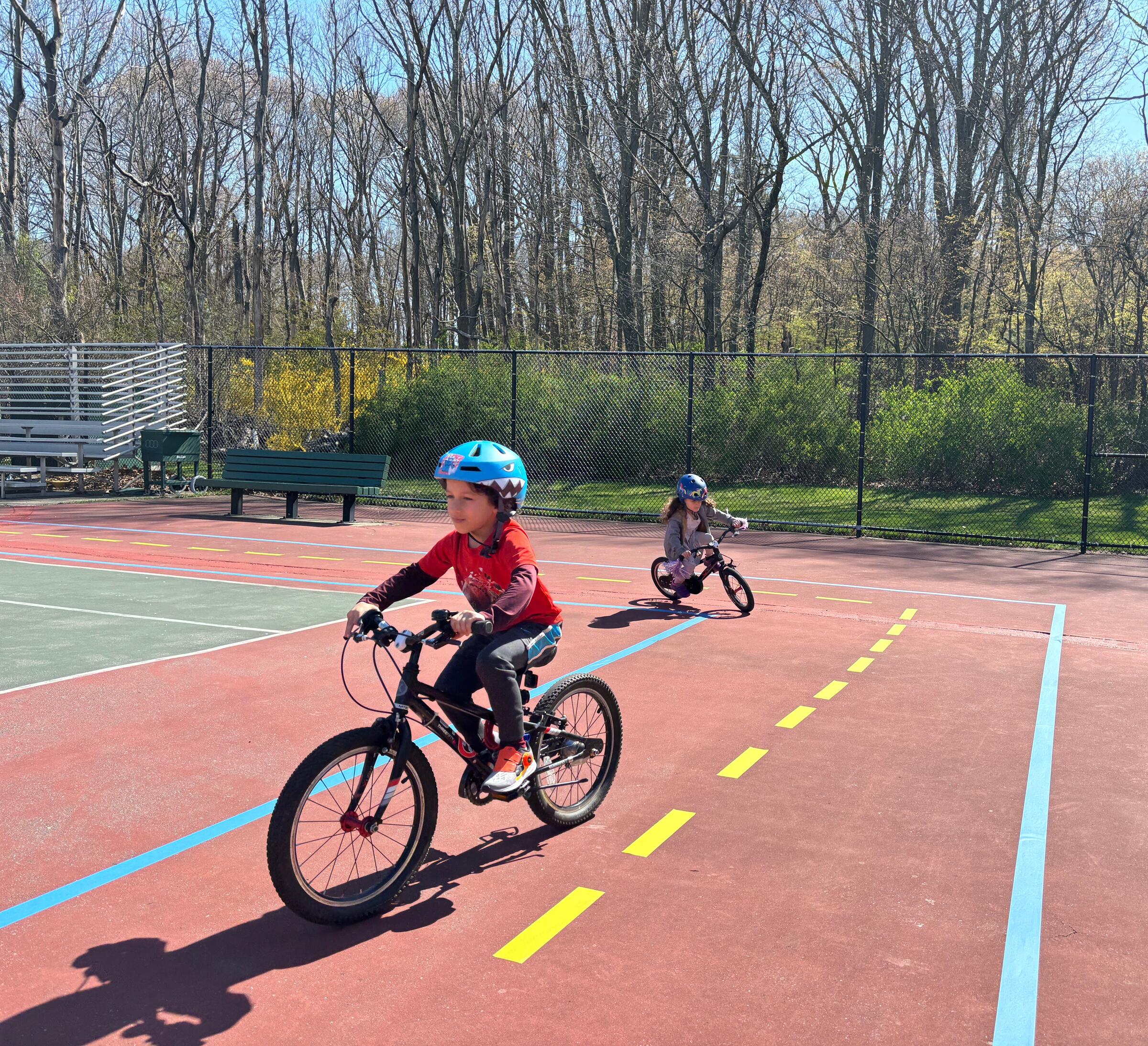 A photo of two children riding bikes on a temporary traffic garden made of painters tape on a tennis court