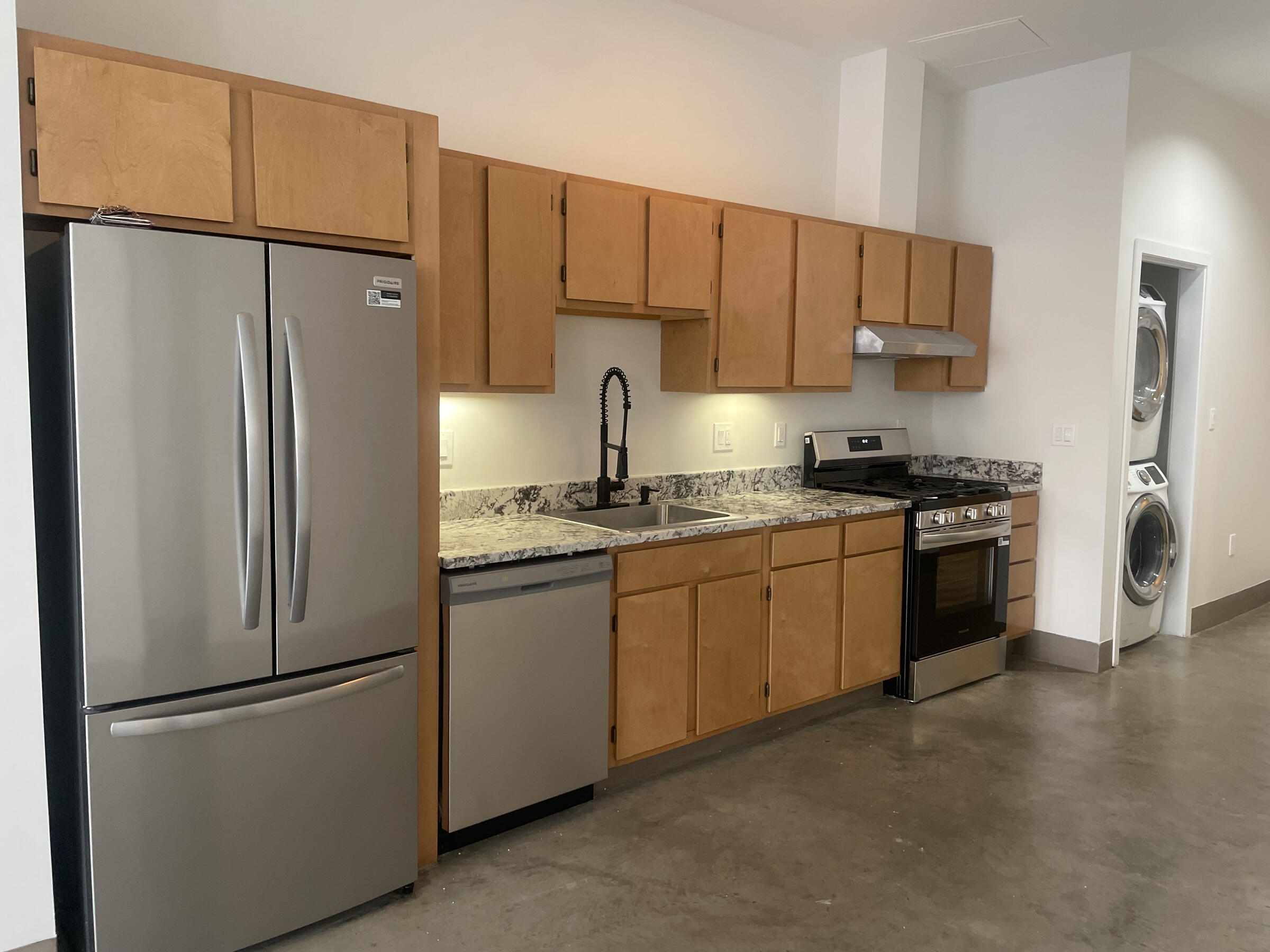 The image is of the kitchen at the 735 Harrison Avenue studio, which is available to certified artists only. The kitchen has cherry cabinets and stainless steel appliances. There is a stackable washer dryer tucked into an alcove. 