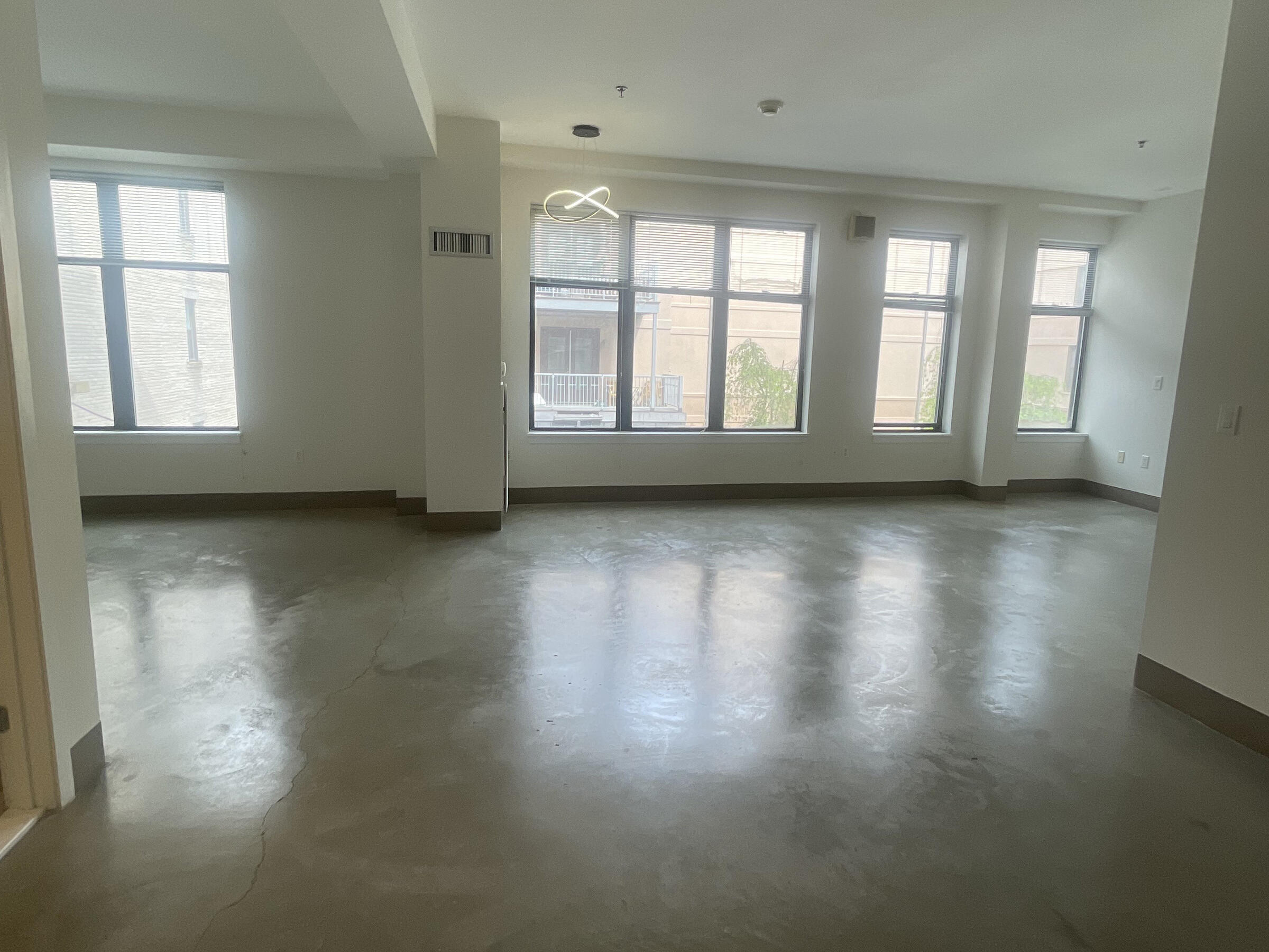 The image is of the work/live space available at the artist studio at 735 Harrison Avenue. The space has several floor to ceiling windows opposite the front door, and also has high-gloss cement floors. 