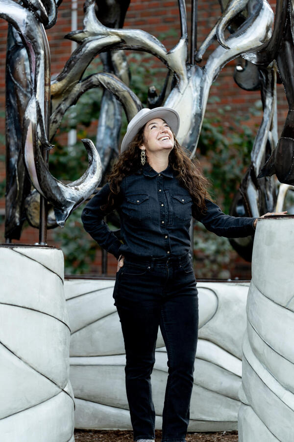 The artist, Rhea Vedro, stands in front of her newly-installed sculpture "Amulet"