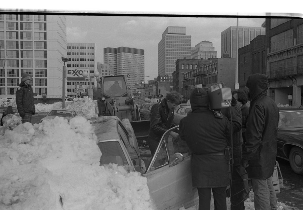  Pedestrians and camera crew in front of car buried in snow on Cambridge Street