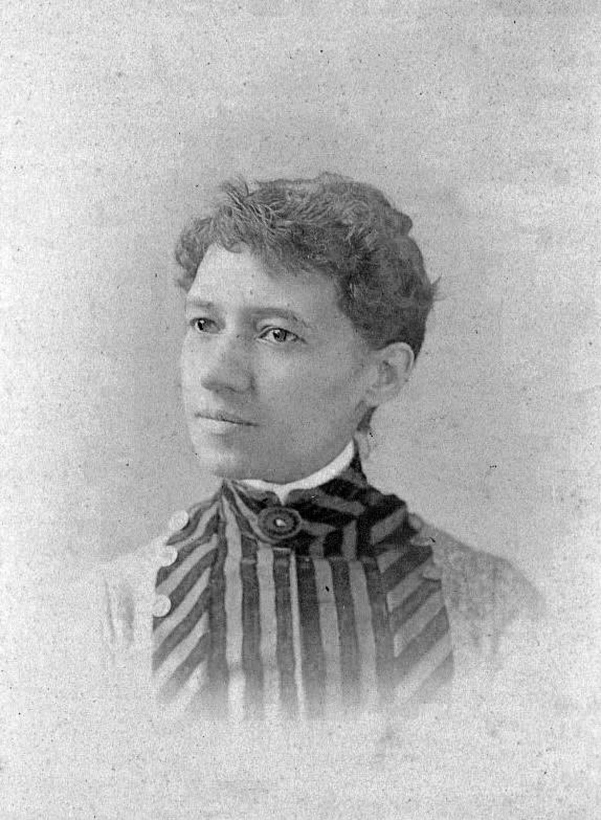 An 1885 photographic portrait of Maria Baldwin. She's wearing a dress with dark and light vertical and diagonal stripes.