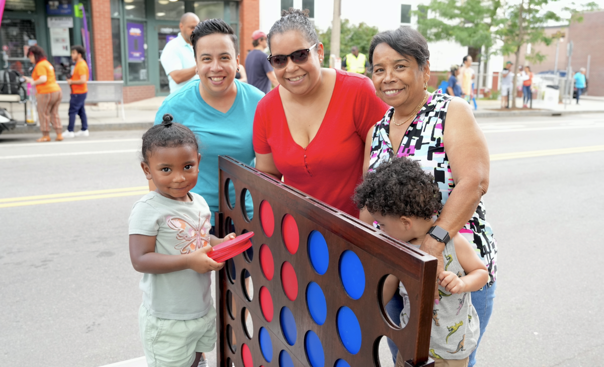 A family of three adults and two children play a large game of connect four