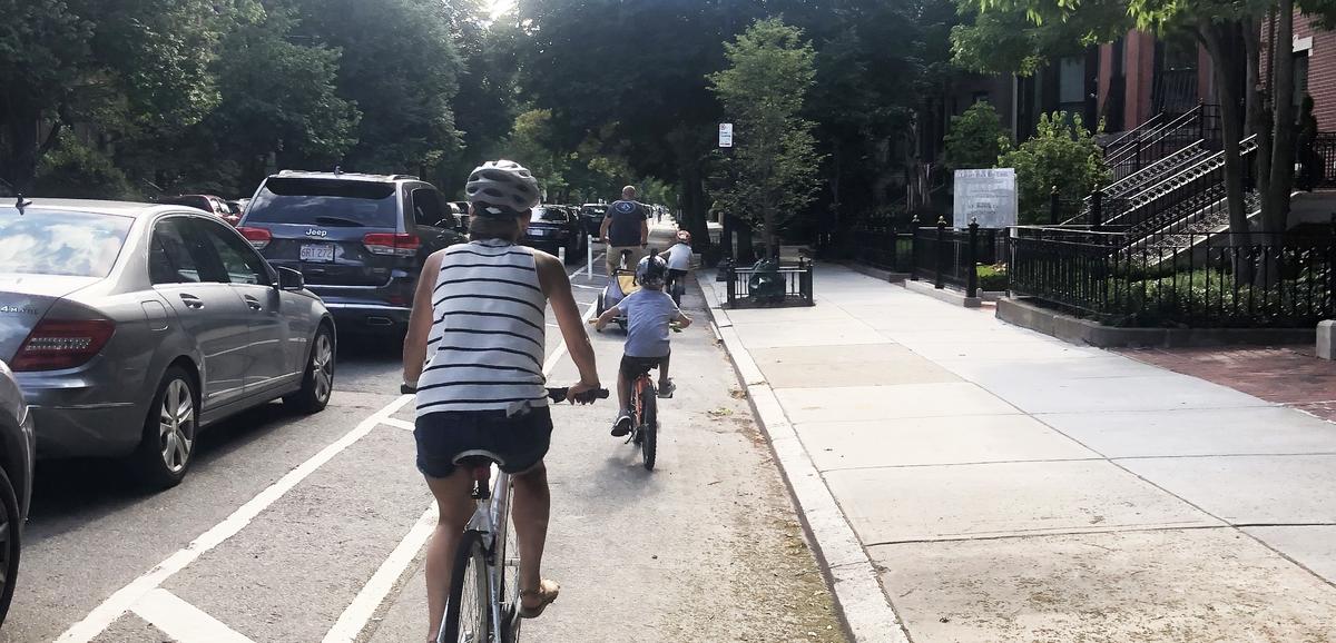 A family rides bikes together in a separated bike lane on Beacon Street