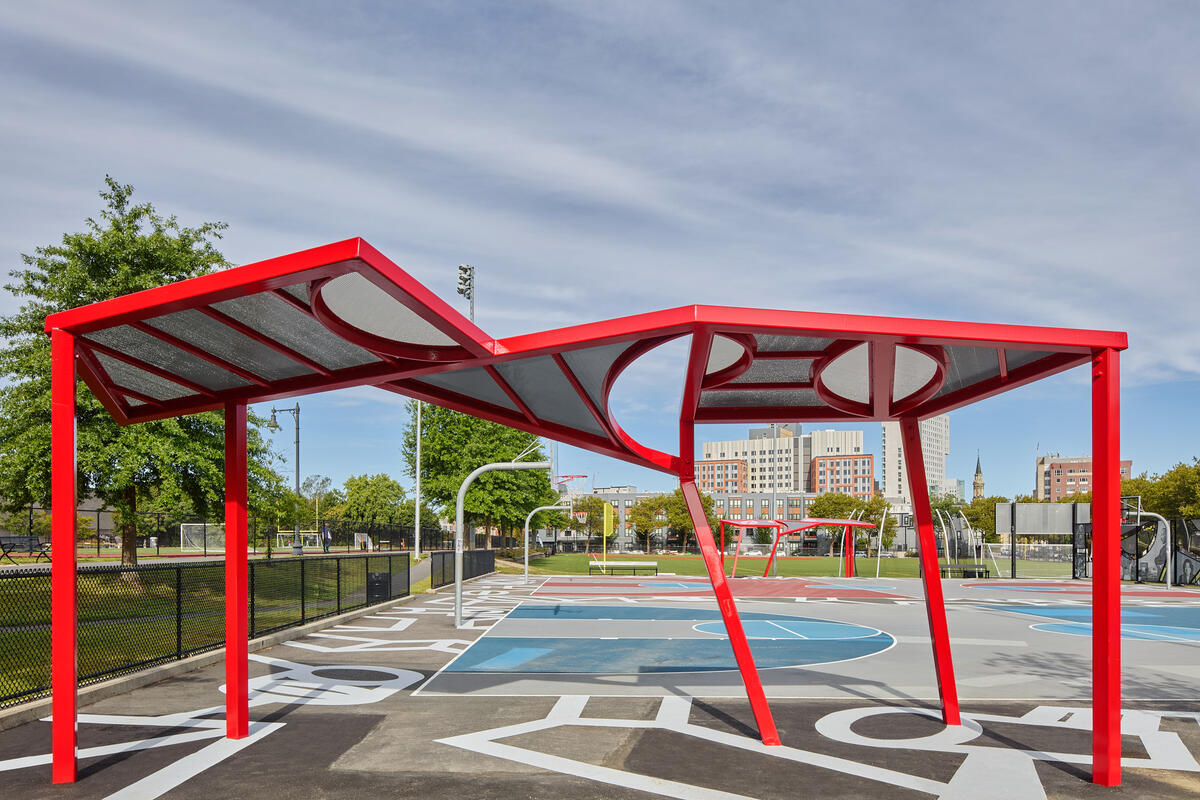 A red, geometric canopy providing shade on the side of a basketball court
