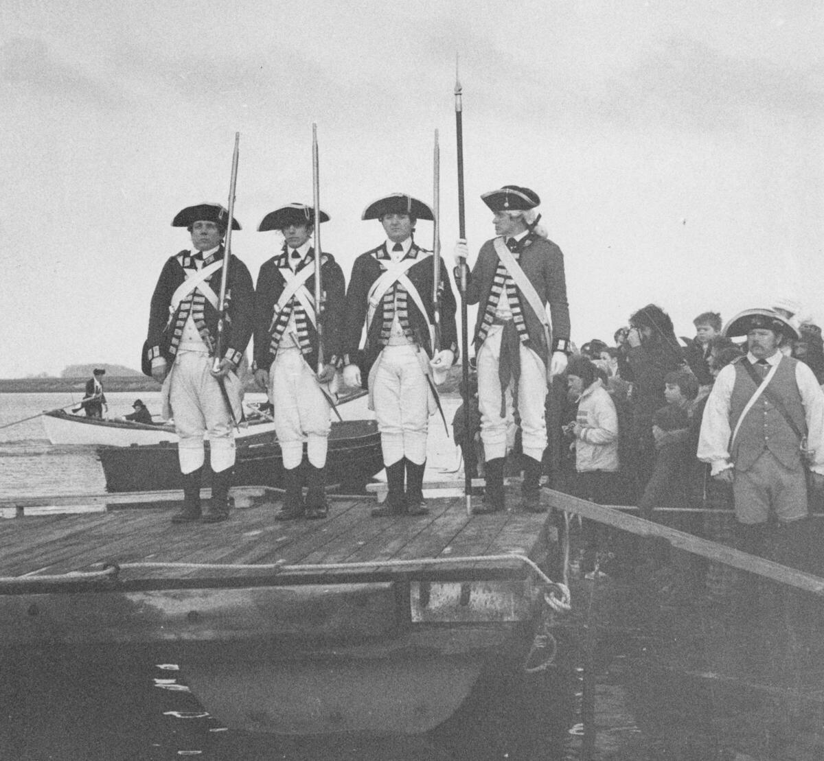 Individuals dressed as British soldiers standing on a dock during the 1976 Evacuation Day celebration