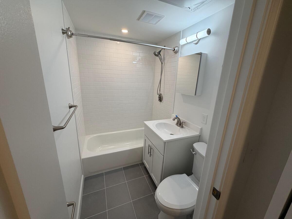 Small, bright bathroom with combination tub and shower, vanity with storage, and gray tiles. 
