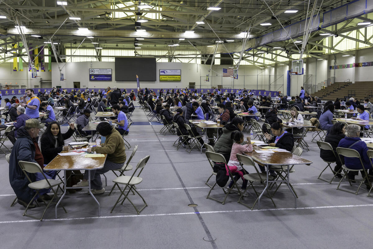 Photo depicting a large community center with many tables. People are receiving legal help related to immigration at each table