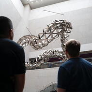 two people seen from behind watching a sculpture being installed 