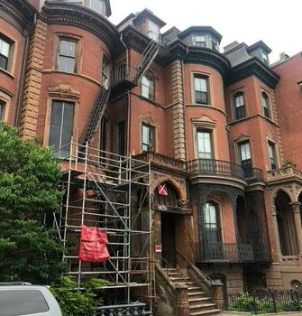 View of the front façade of an ornate 1850s South End brownstone building with scaffolding on the outside