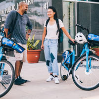 A man and a women stand together outside the Grove Hall library. Each person has a bike share bike next to them.